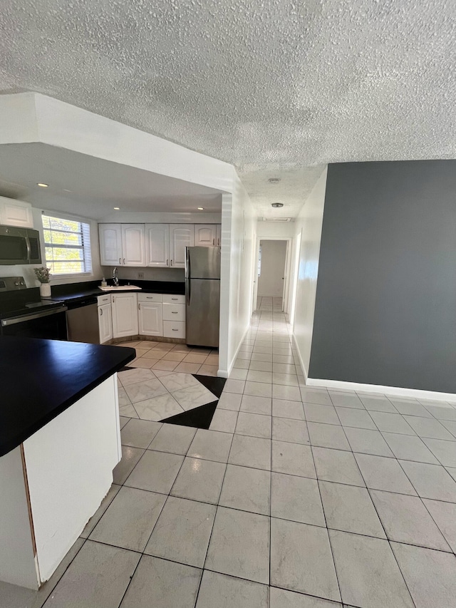 kitchen with stainless steel appliances, light tile patterned flooring, white cabinetry, sink, and a textured ceiling