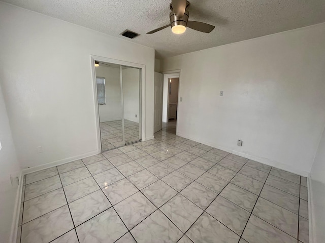 unfurnished bedroom with light tile patterned floors, ceiling fan, a textured ceiling, and a closet