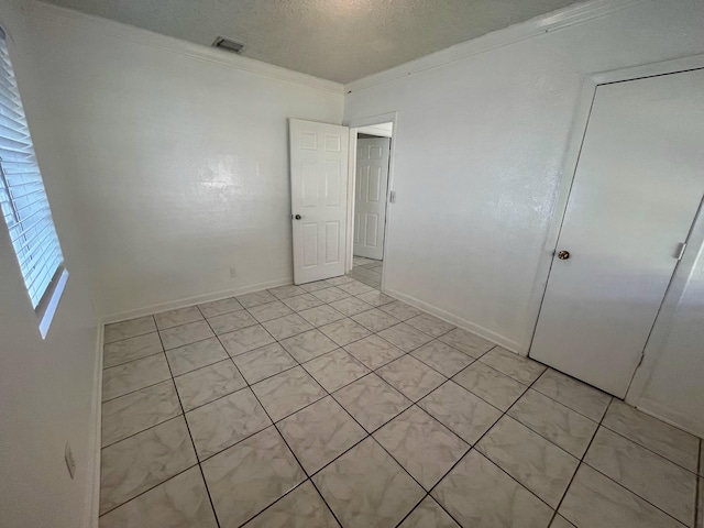 unfurnished bedroom featuring a textured ceiling, light tile patterned flooring, crown molding, and a closet