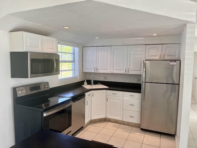 kitchen featuring vaulted ceiling, white cabinets, sink, light tile patterned floors, and appliances with stainless steel finishes