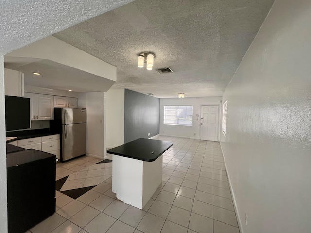 kitchen with white cabinets, kitchen peninsula, a textured ceiling, light tile patterned floors, and stainless steel refrigerator