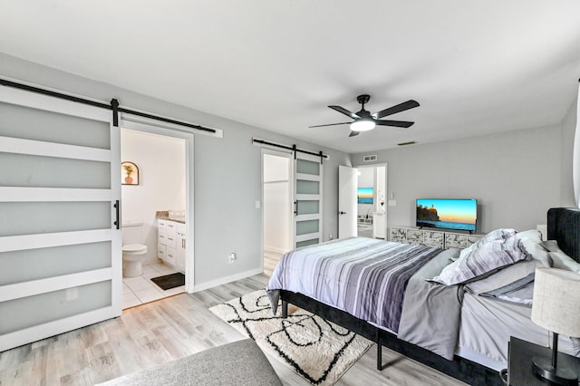 bedroom with ceiling fan, a barn door, light hardwood / wood-style floors, and ensuite bathroom