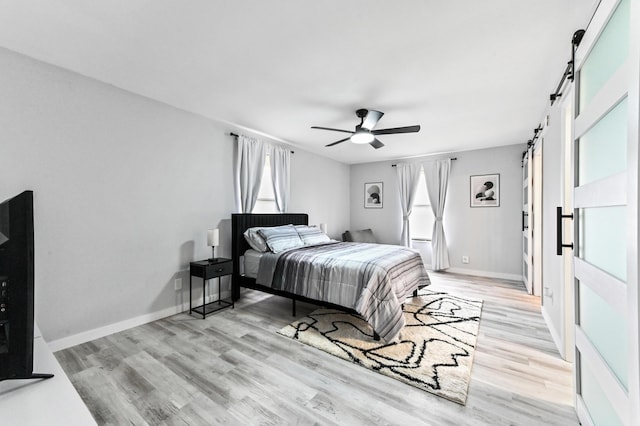 bedroom featuring multiple windows, a barn door, light hardwood / wood-style flooring, and ceiling fan