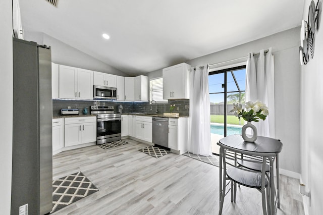 kitchen featuring backsplash, white cabinetry, lofted ceiling, and appliances with stainless steel finishes