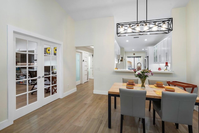 dining area featuring french doors, a notable chandelier, light hardwood / wood-style floors, and a high ceiling