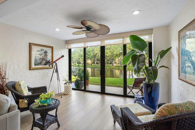 interior space featuring a textured ceiling, a water view, light hardwood / wood-style floors, and ceiling fan