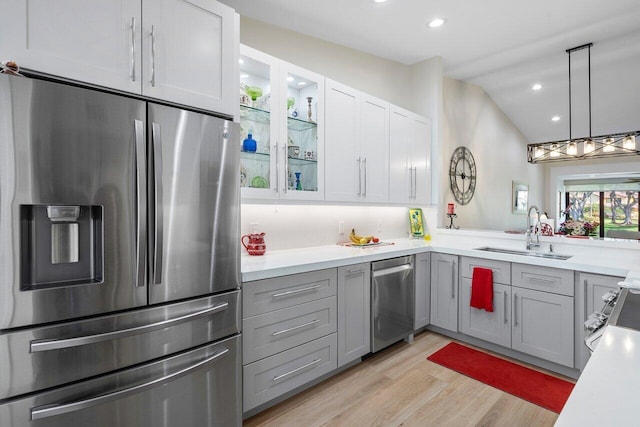 kitchen featuring appliances with stainless steel finishes, sink, light wood-type flooring, vaulted ceiling, and white cabinets