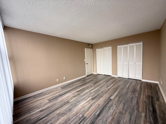 unfurnished bedroom with dark hardwood / wood-style floors, a textured ceiling, and multiple closets