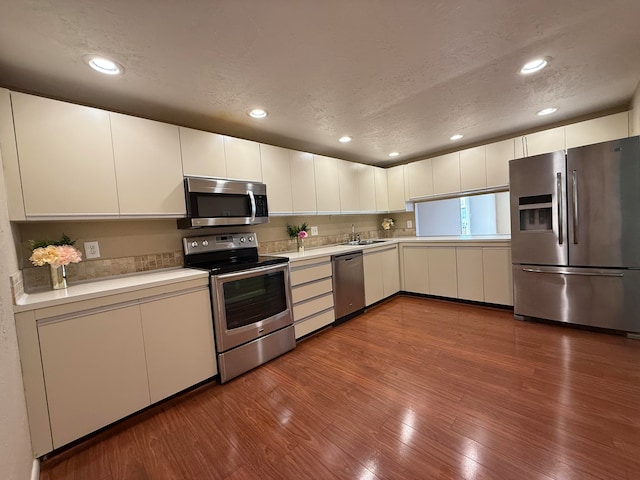 kitchen featuring wood-type flooring, sink, a textured ceiling, appliances with stainless steel finishes, and white cabinetry