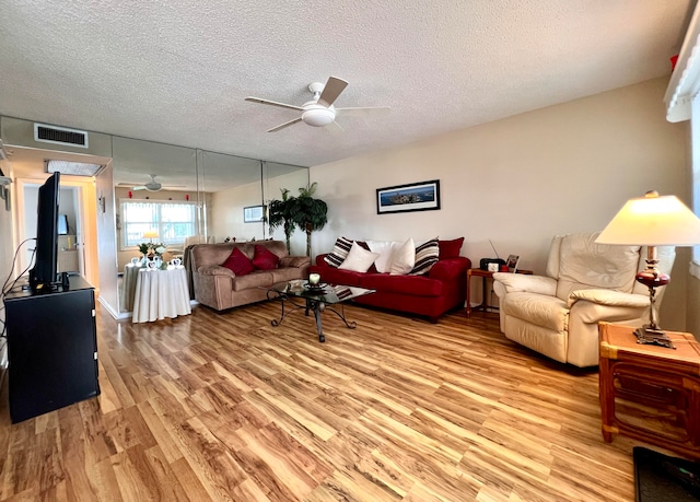 living room featuring ceiling fan, a textured ceiling, and light hardwood / wood-style flooring