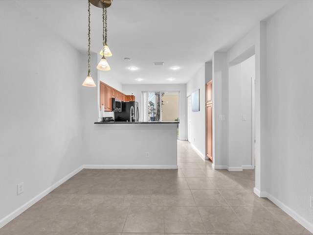 kitchen featuring pendant lighting, light tile patterned floors, kitchen peninsula, and stainless steel refrigerator