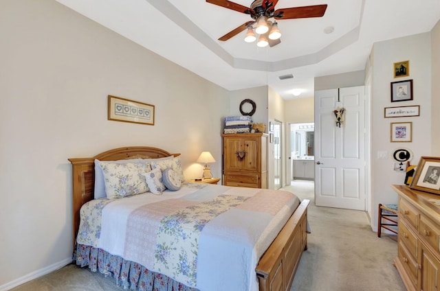 bedroom featuring a tray ceiling, light colored carpet, connected bathroom, and ceiling fan