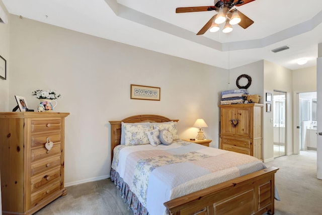 bedroom featuring light colored carpet, a tray ceiling, and ceiling fan