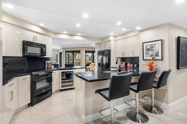 kitchen featuring kitchen peninsula, beverage cooler, white cabinetry, a kitchen bar, and black appliances