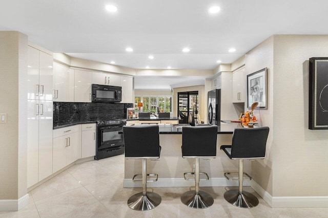 kitchen featuring kitchen peninsula, backsplash, black appliances, a kitchen bar, and white cabinets