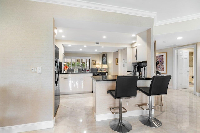 kitchen featuring kitchen peninsula, ornamental molding, a breakfast bar, stainless steel fridge, and white cabinetry