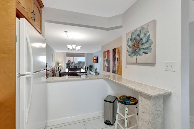 kitchen featuring kitchen peninsula, a textured ceiling, light stone countertops, a chandelier, and white refrigerator