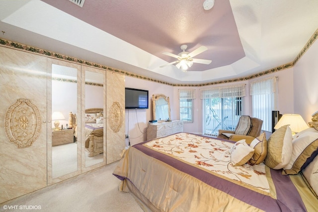 bedroom featuring light carpet, a closet, a tray ceiling, and ceiling fan