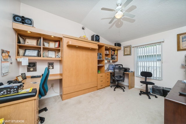 home office featuring lofted ceiling, built in desk, light colored carpet, a textured ceiling, and ceiling fan