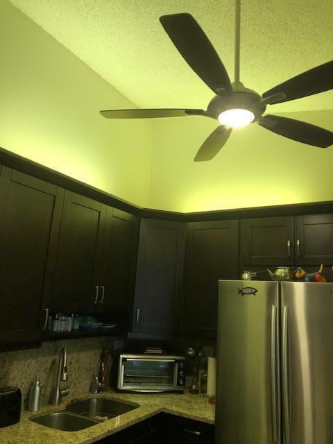 kitchen featuring decorative backsplash, ceiling fan, light stone countertops, stainless steel refrigerator, and sink