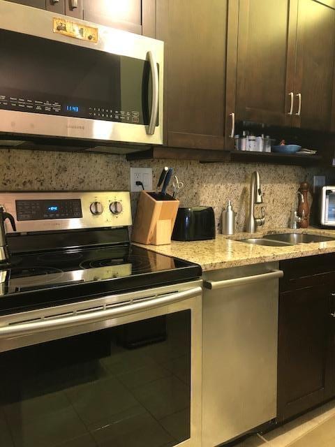 kitchen with light stone countertops, appliances with stainless steel finishes, sink, dark brown cabinets, and light tile patterned floors