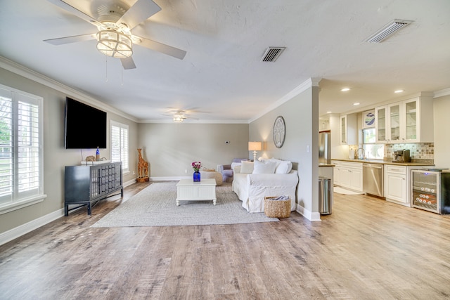 living room with light hardwood / wood-style flooring, ornamental molding, beverage cooler, and a wealth of natural light