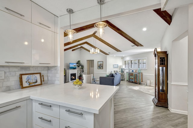 kitchen with tasteful backsplash, vaulted ceiling with beams, pendant lighting, white cabinets, and light stone counters