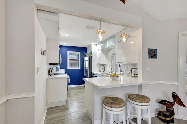 kitchen featuring light wood-type flooring, a textured ceiling, kitchen peninsula, decorative light fixtures, and white cabinets