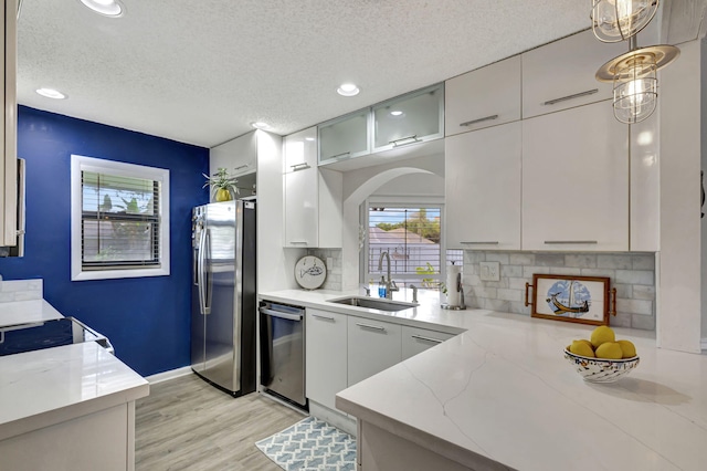 kitchen featuring hanging light fixtures, sink, appliances with stainless steel finishes, light stone counters, and a textured ceiling