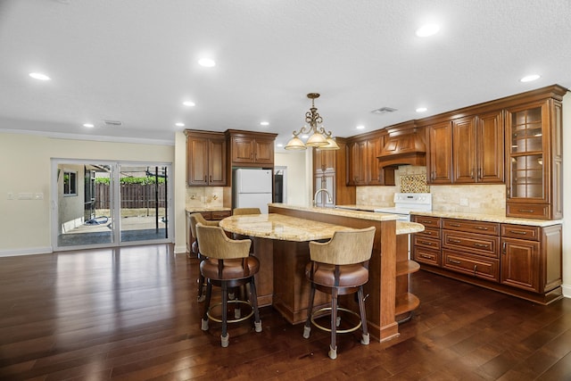 100 SW 15th Ct, Boca Raton, FL 33486 - kitchen featuring white appliances, premium range hood, backsplash, an island with sink, and light stone countertops
