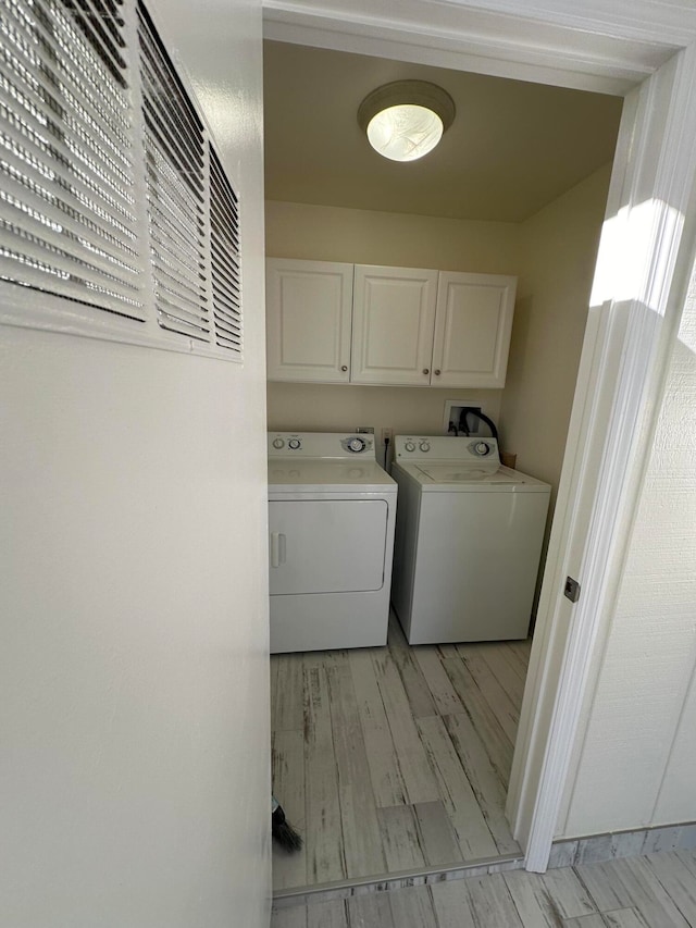 laundry room with cabinets, light wood-type flooring, and washing machine and clothes dryer