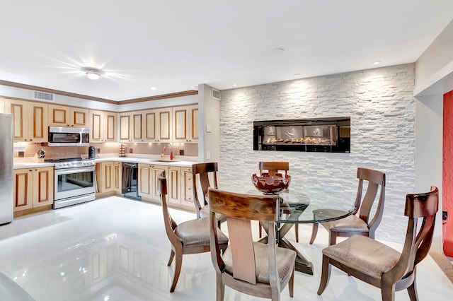 kitchen with light brown cabinets, ornamental molding, sink, a fireplace, and stainless steel appliances