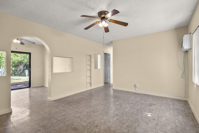 empty room featuring built in shelves, a wall unit AC, a textured ceiling, and ceiling fan