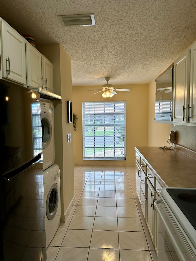 kitchen with stacked washer and dryer, fridge, light tile patterned floors, white cabinets, and ceiling fan