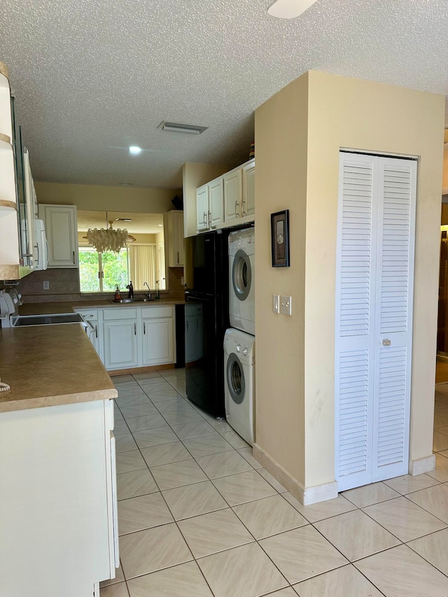 kitchen with stacked washer / drying machine, white cabinets, a textured ceiling, and light tile patterned floors