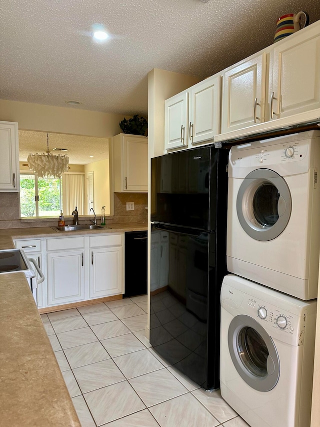 clothes washing area with stacked washer and clothes dryer, sink, light tile patterned floors, a chandelier, and a textured ceiling