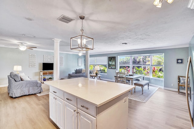 kitchen featuring decorative columns, a center island, pendant lighting, light wood-type flooring, and white cabinetry