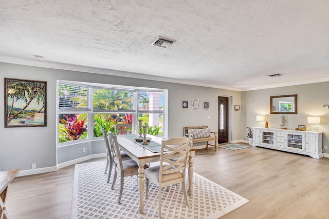 dining space featuring light hardwood / wood-style floors, ornamental molding, and a textured ceiling