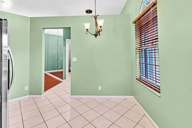 tiled spare room with a textured ceiling and an inviting chandelier