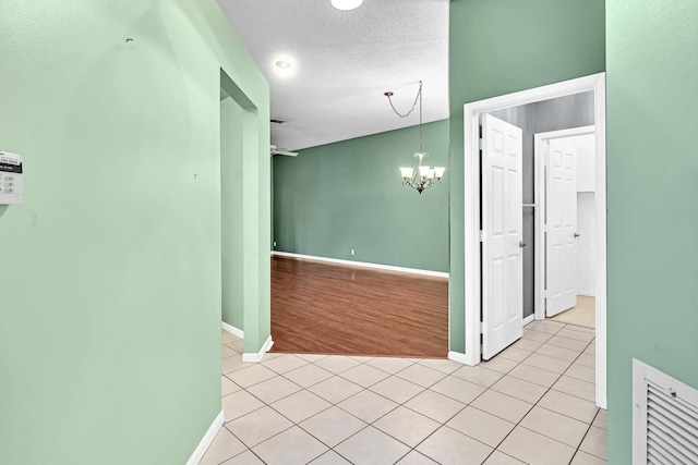 corridor with light hardwood / wood-style flooring, a textured ceiling, and a chandelier