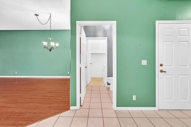 empty room featuring a notable chandelier, a textured ceiling, and light wood-type flooring