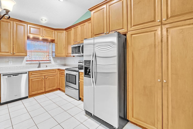 kitchen featuring stainless steel appliances, lofted ceiling, light tile patterned floors, and a textured ceiling