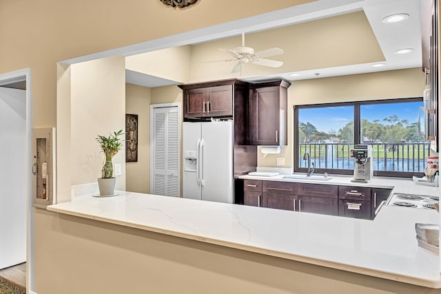 kitchen with kitchen peninsula, ceiling fan, light stone countertops, sink, and white refrigerator with ice dispenser