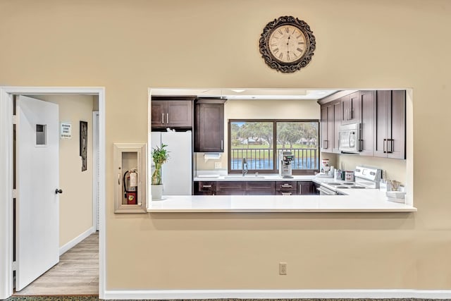 kitchen with light hardwood / wood-style floors, kitchen peninsula, dark brown cabinets, and white appliances