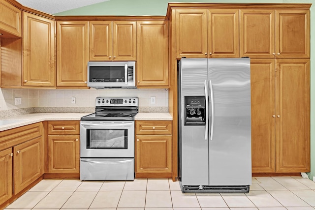 kitchen with appliances with stainless steel finishes, sink, light tile patterned flooring, backsplash, and vaulted ceiling