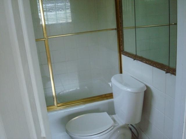 bathroom featuring toilet, tile walls, and enclosed tub / shower combo