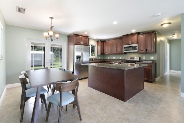 kitchen with dark stone countertops, a center island, an inviting chandelier, hanging light fixtures, and appliances with stainless steel finishes