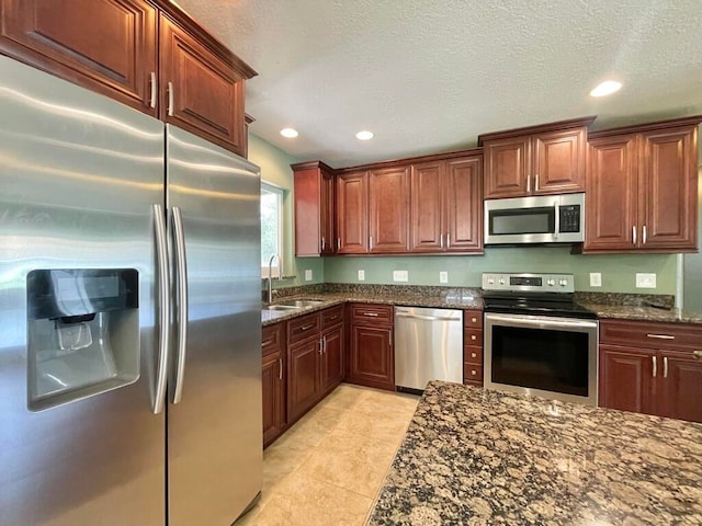 kitchen with sink, stainless steel appliances, a textured ceiling, light tile patterned floors, and dark stone counters