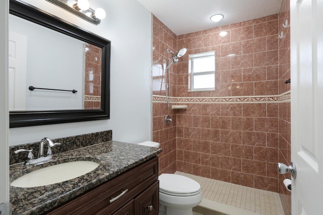 bathroom with toilet, tiled shower, and vanity