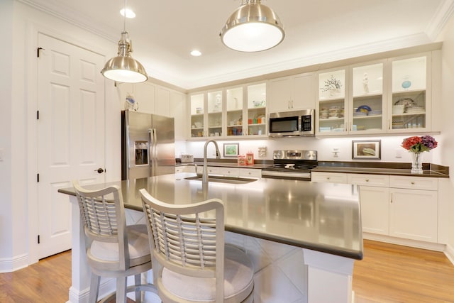 kitchen featuring appliances with stainless steel finishes, a kitchen island with sink, sink, light hardwood / wood-style floors, and decorative light fixtures